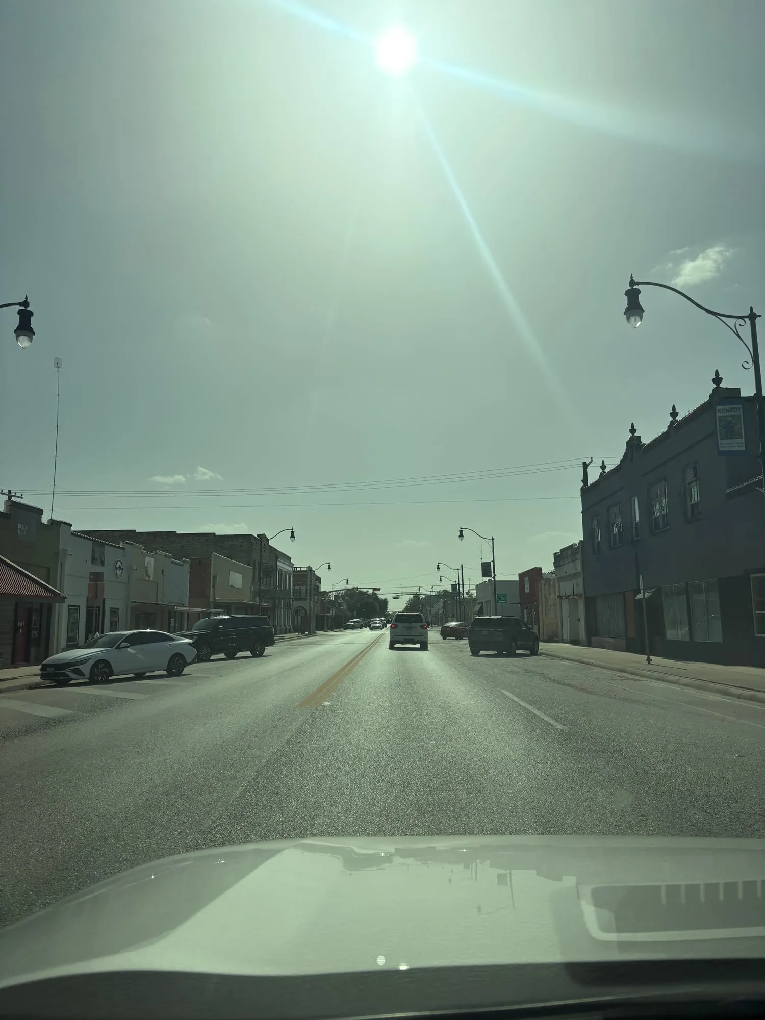 Wide small town main street with low brick storefronts, ornate street lamps, and a banner reading Kenedy on the corner building