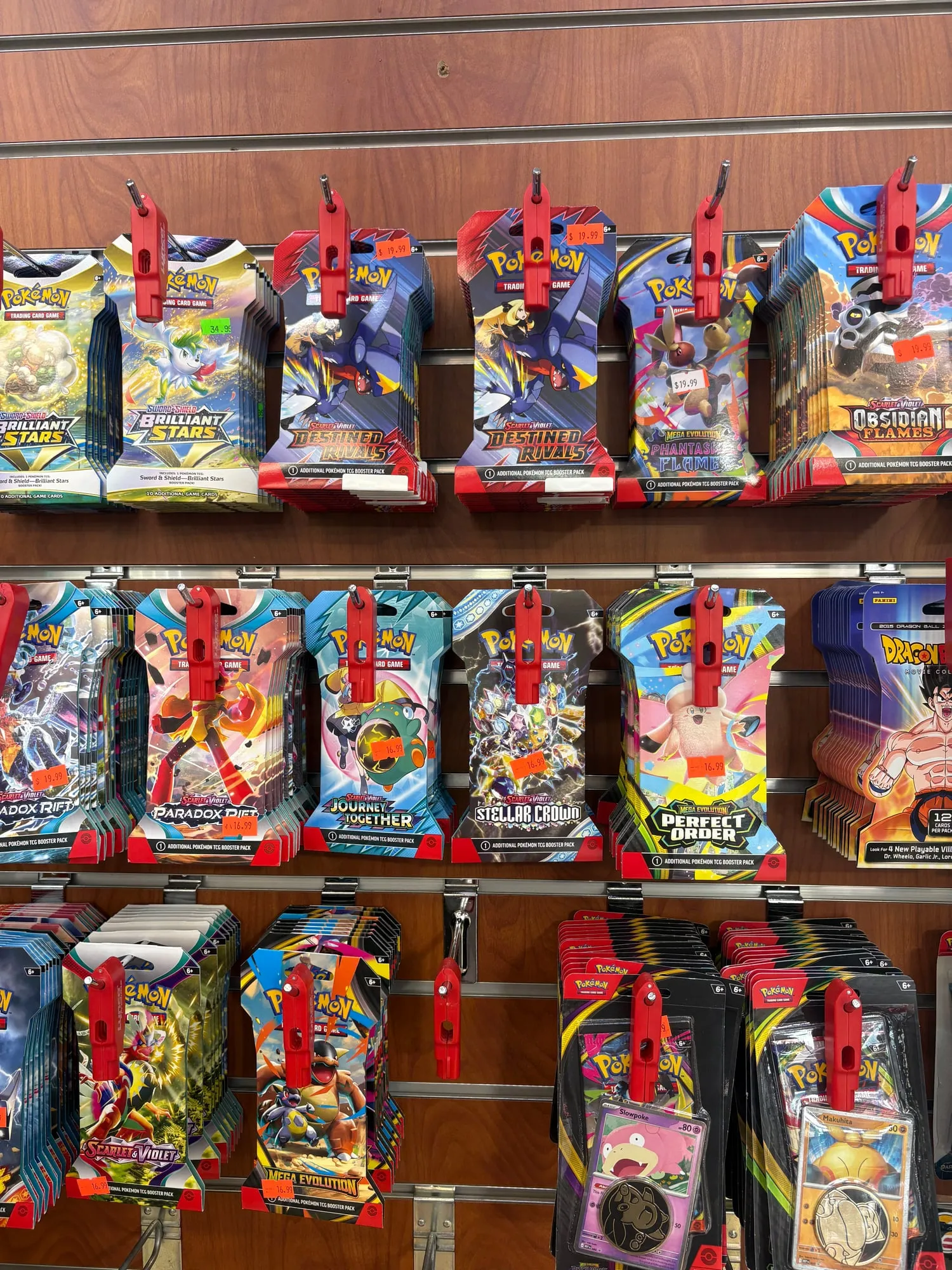 Pegboard wall hung with rows of Pokémon trading card booster packs and blister packs, orange price tags on each hook