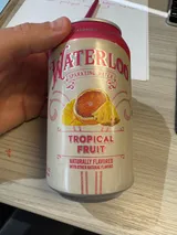 Waterloo Tropical Fruit sparkling water can held over a desk with handwritten notes in the background